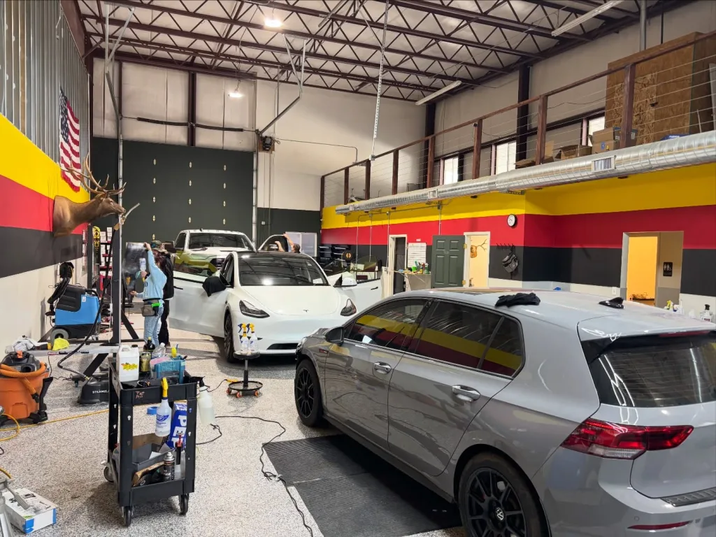 Cars on the floor at Black Optix Tint West Haven, mid-install against the shop's striped wall